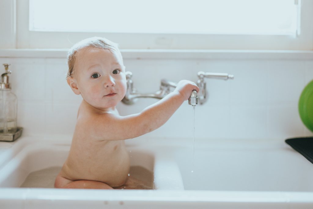 A baby getting a bath in a kitchen sink. 