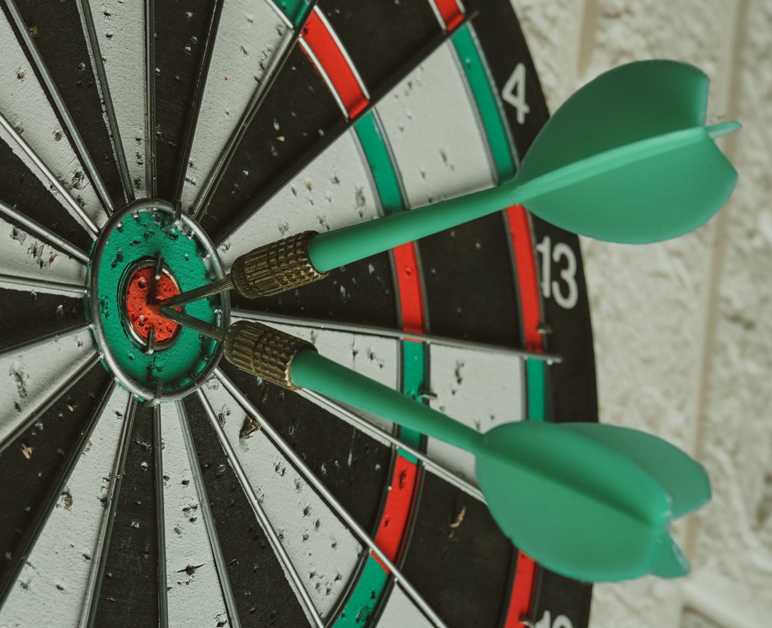 Dart board with two green darts in the bullseye.