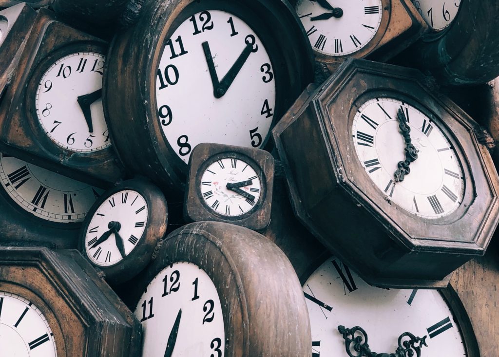 Image of a pile of clocks, each showing a different time of day. 