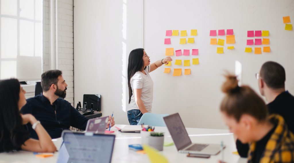 Photo image of woman placing sticky notes on a whiteboard during team meeting.