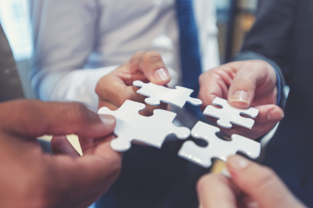 Four hands converging, each holding a puzzle piece. 