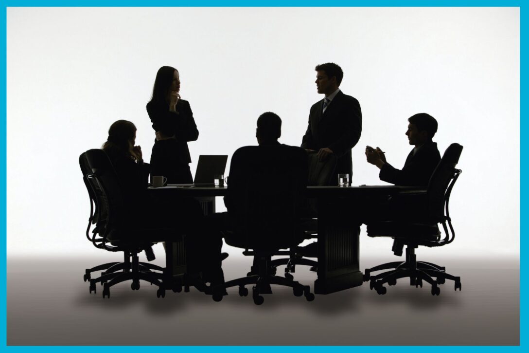 office workers sitting and standing around a table having a meeting