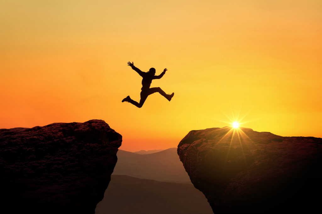 Silhouette of a man jumping across a chasm.